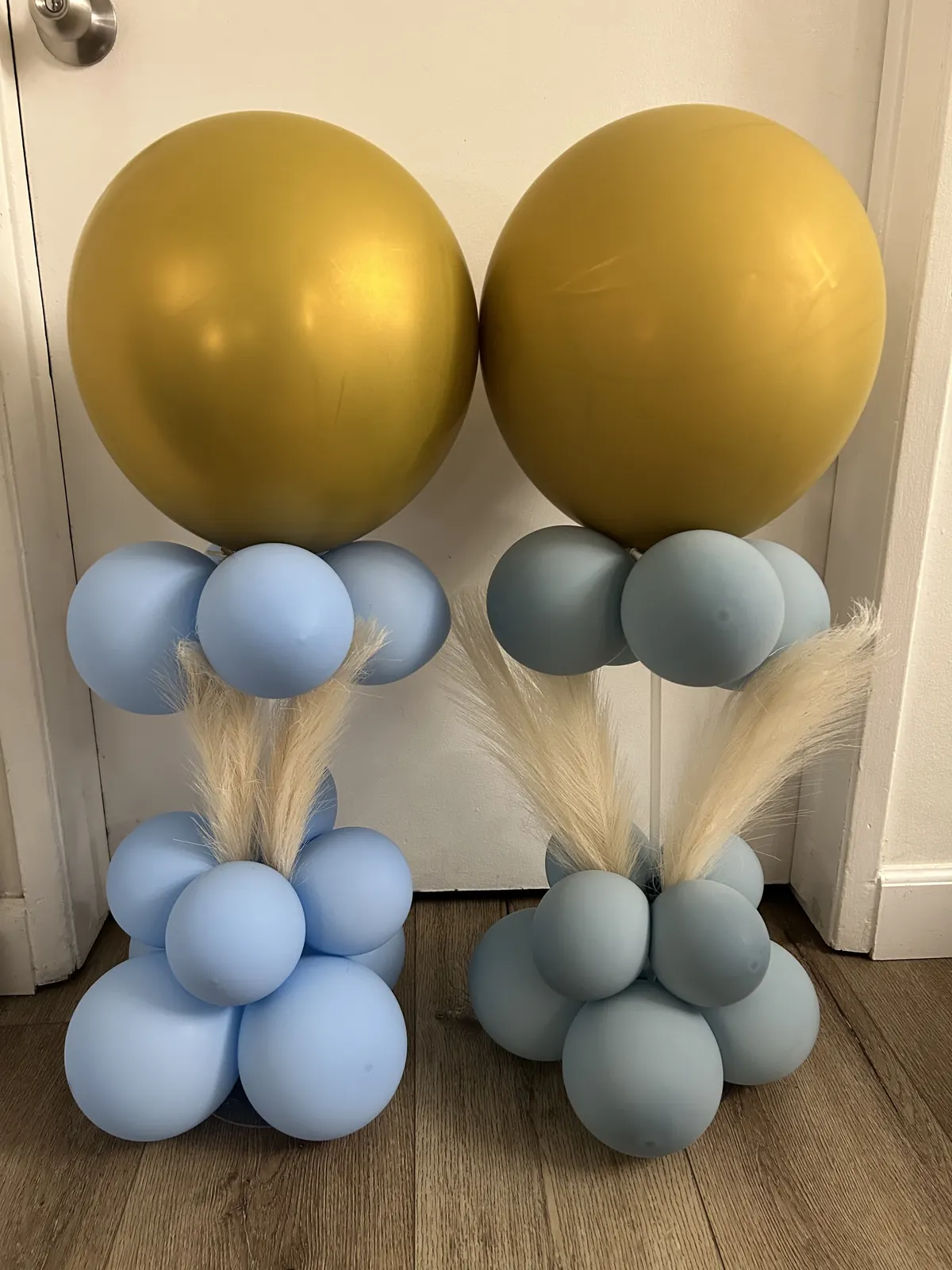 Two balloon centerpieces with a gold topper, dusty blue balloons and pampas grass