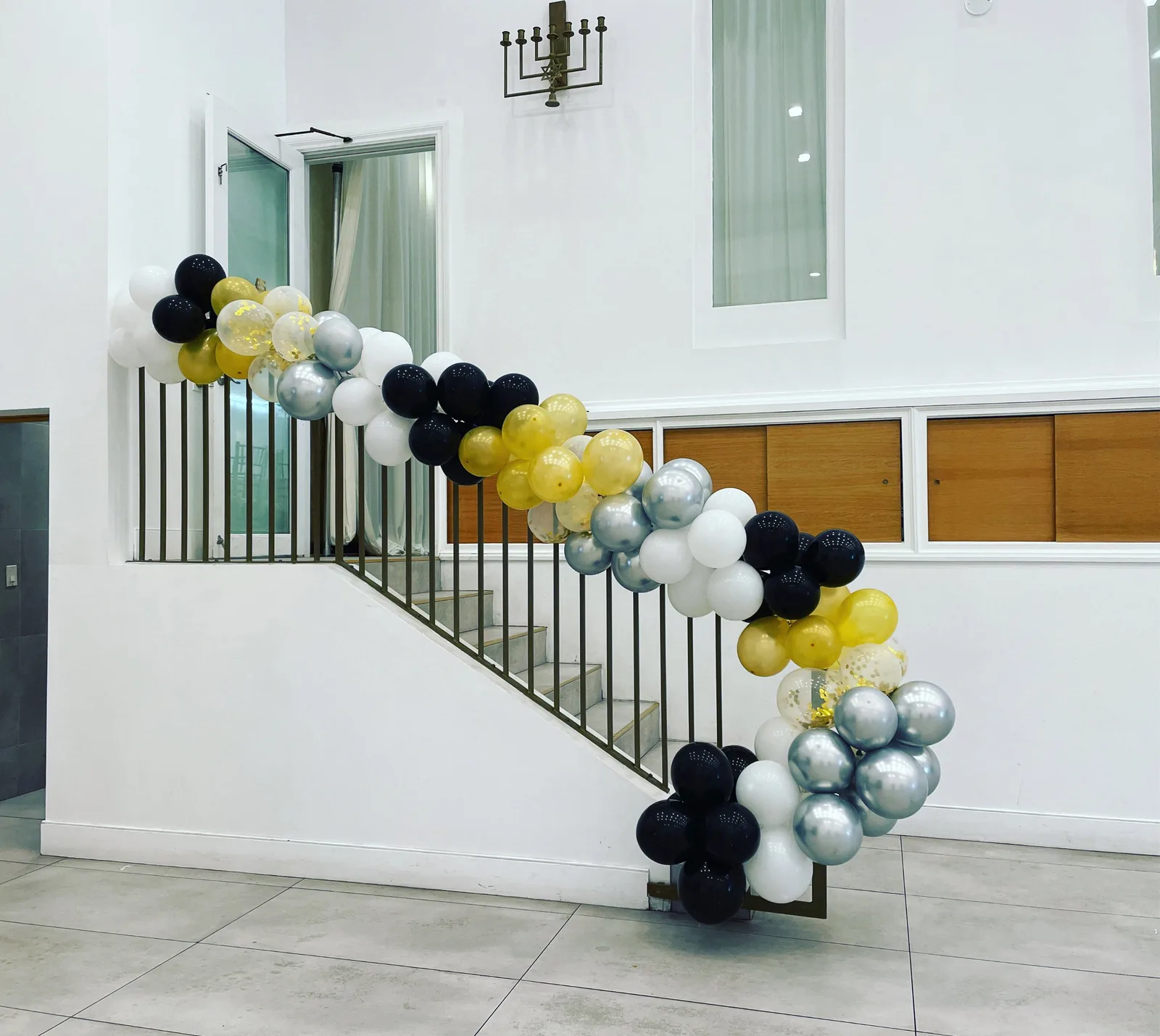 Black, gold, silver and white balloon garland with gold confetti balloons running down a staircase railing