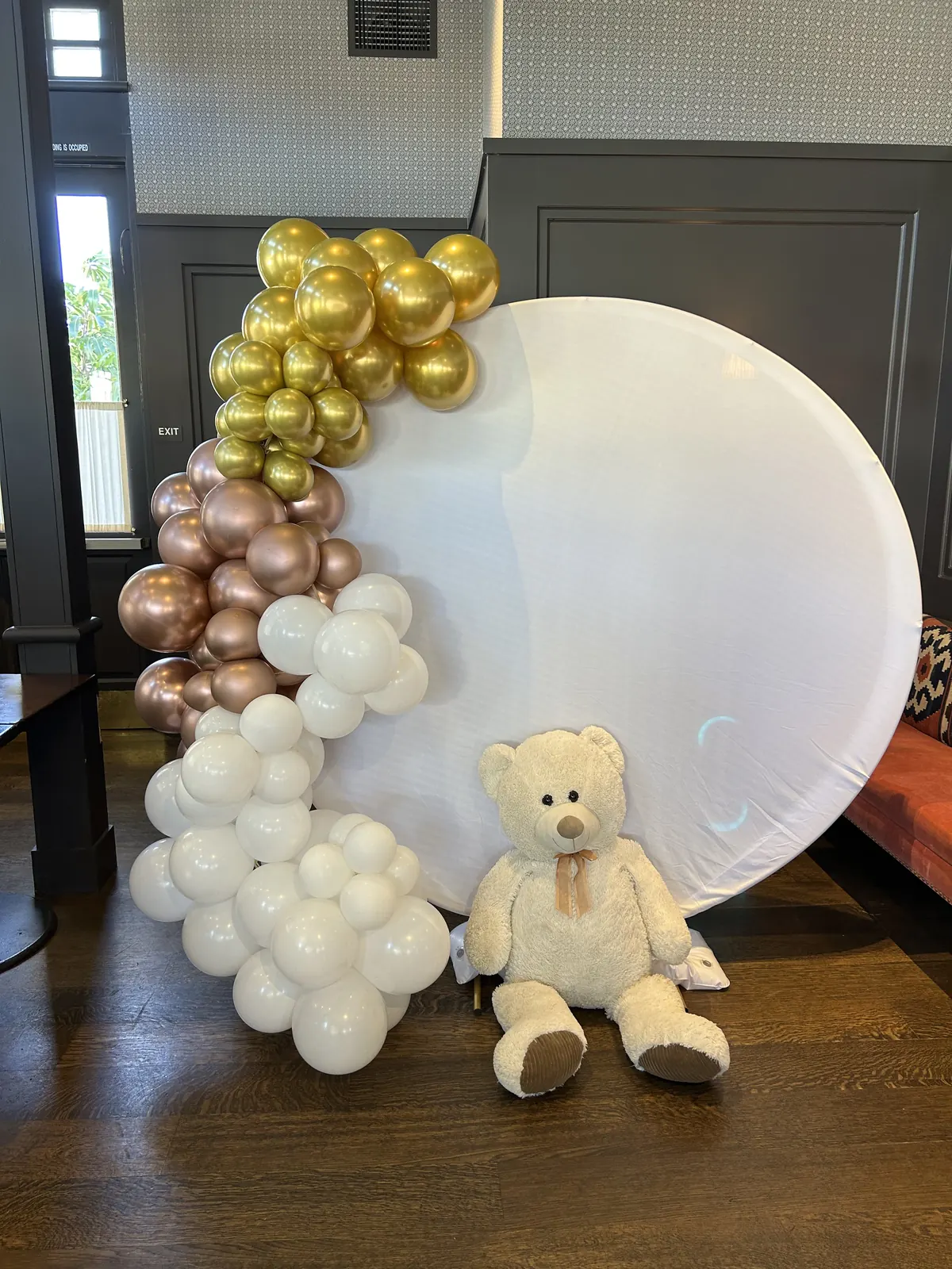 Round white backdrop with gold, rose gold and white balloons and a teddy bear