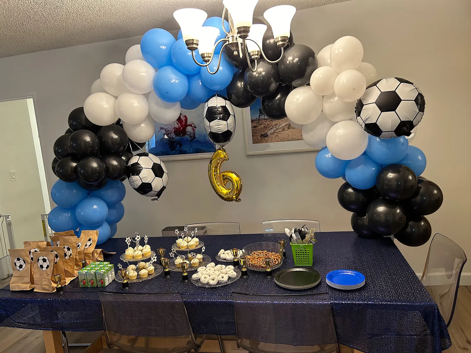 Soccer-themed table balloon arch in blue, black and white over a sixth birthday dessert table